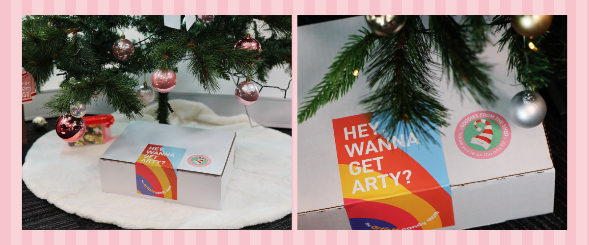 Close-up of Art Shed’s custom Christmas sticker printed by OzStickerPrinting on a parcel beneath a decorated Christmas tree